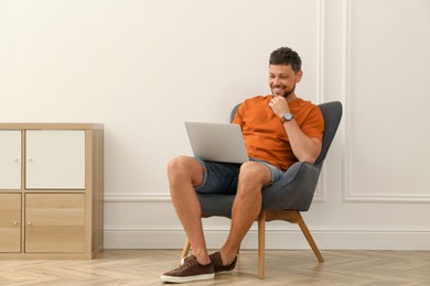 Photo of Happy man using laptop in armchair at home. Internet shopping