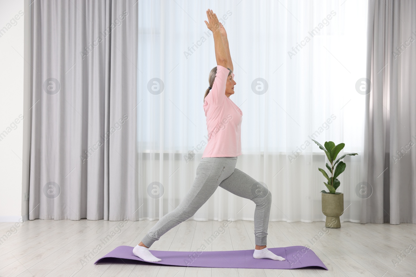 Photo of Senior woman practicing yoga on mat at home