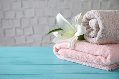Photo of Folded clean soft bath towels and beautiful flower on blue wooden table. Space for text