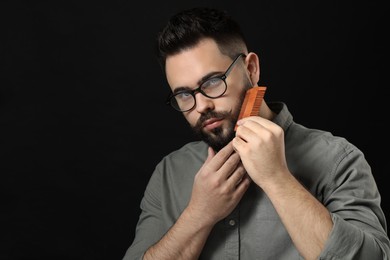 Photo of Handsome young man combing beard on black background. Space for text