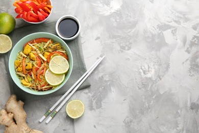 Photo of Stir-fry. Delicious cooked noodles with chicken and vegetables in bowl served on gray textured table, flat lay. Space for text