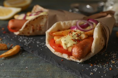 Photo of Delicious pita wrap with sausages, vegetables and potato fries on dark wooden table, closeup