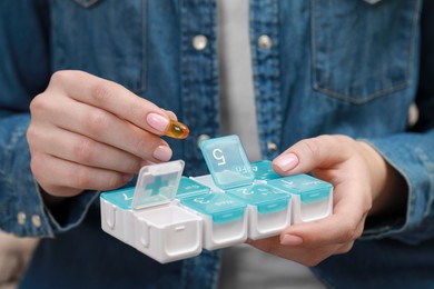 Woman taking pill from plastic box indoors, closeup