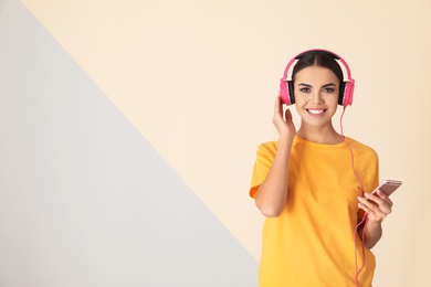 Photo of Attractive woman with mobile phone enjoying music in headphones on color background. Space for text
