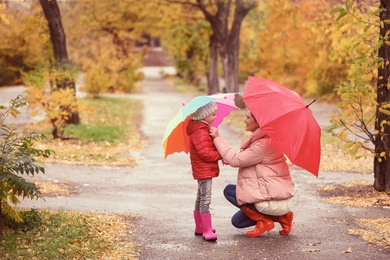 Mother and daughter with umbrellas taking walk in autumn park on rainy day