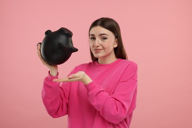 Sad woman with piggy bank on pink background