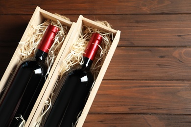 Photo of Bottles with delicious red wine in boxes on wooden background, top view