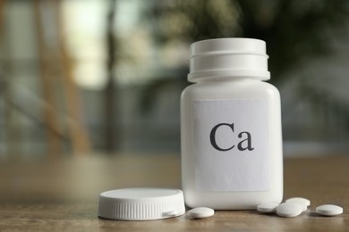 Photo of Bottle of calcium supplement pills on wooden table against blurred background. Space for text
