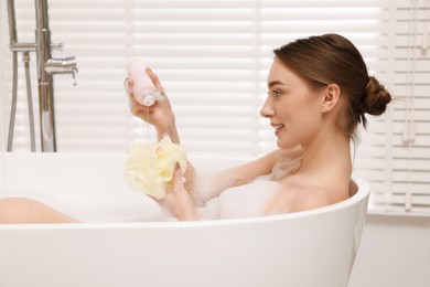 Photo of Woman pouring shower gel onto mesh pouf in bath indoors