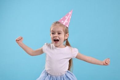 Photo of Birthday celebration. Cute little girl in party hat on light blue background