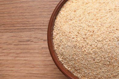 Fresh bread crumbs in bowl on wooden table, top view. Space for text