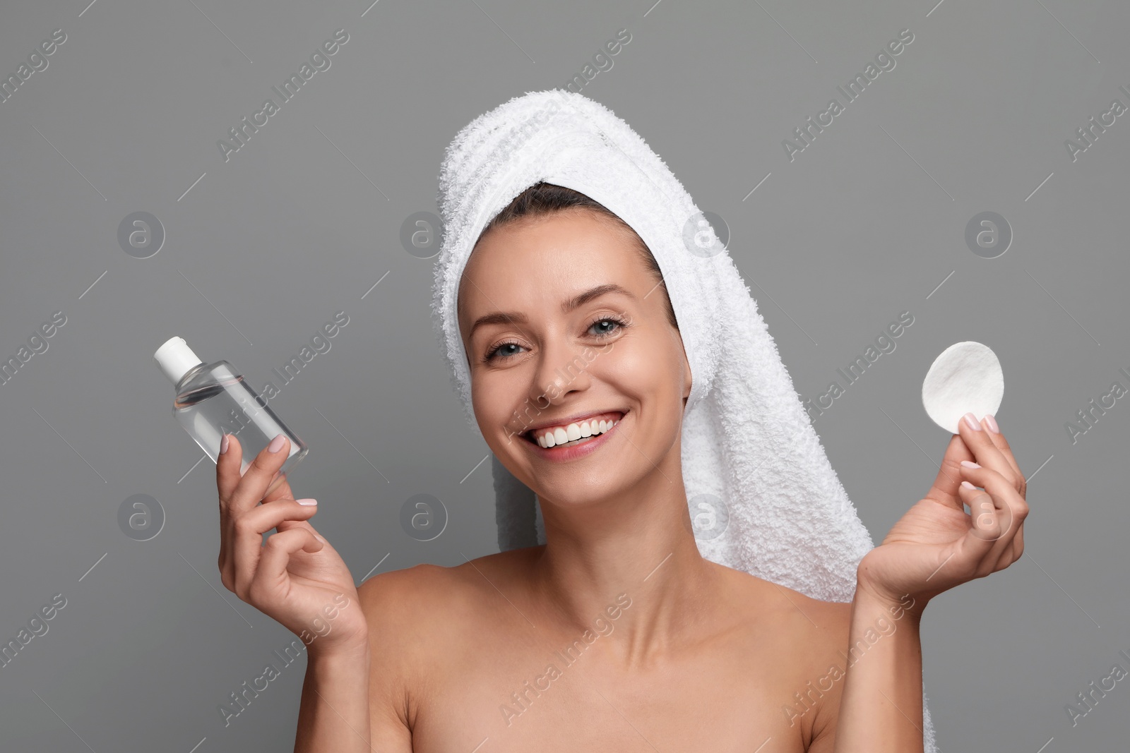 Photo of Removing makeup. Smiling woman with cotton pad and bottle on grey background