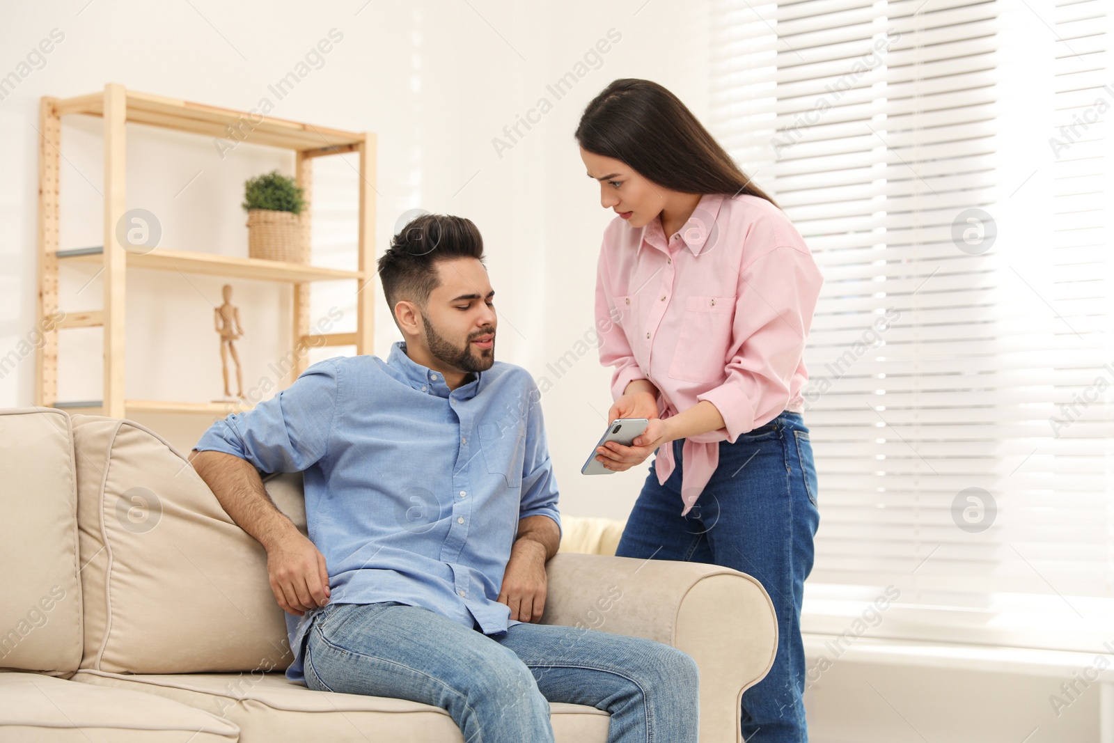 Photo of Young couple arguing about smartphone at home. Problems in relationship