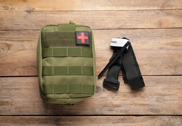 Military first aid kit and tourniquet on wooden table, flat lay