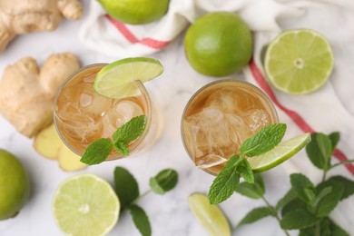 Photo of Glasses of tasty ginger ale with ice cubes and ingredients on white marble table, flat lay