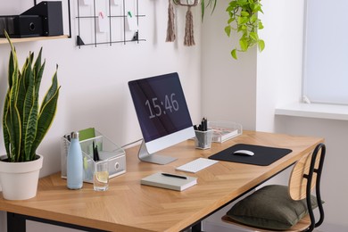 Cozy workplace with computer, modern furniture and houseplants at home