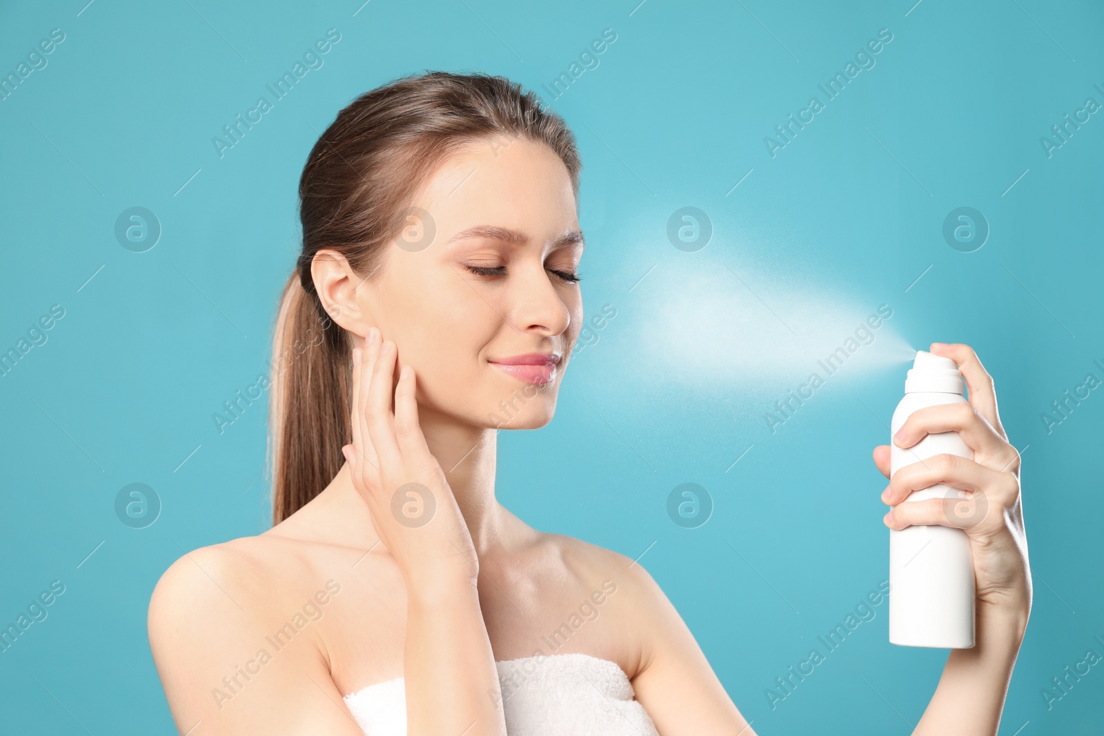 Photo of Young woman applying thermal water on face against color background. Cosmetic product