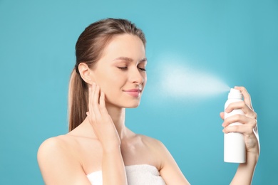 Photo of Young woman applying thermal water on face against color background. Cosmetic product