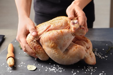 Photo of Woman preparing whole turkey at table, closeup