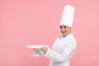 Photo of Happy professional confectioner in uniform holding empty cake stand on pink background. Space for text