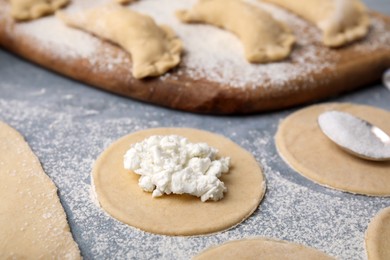 Photo of Process of making dumplings (varenyky) with cottage cheese. Raw dough and ingredients on grey table, closeup