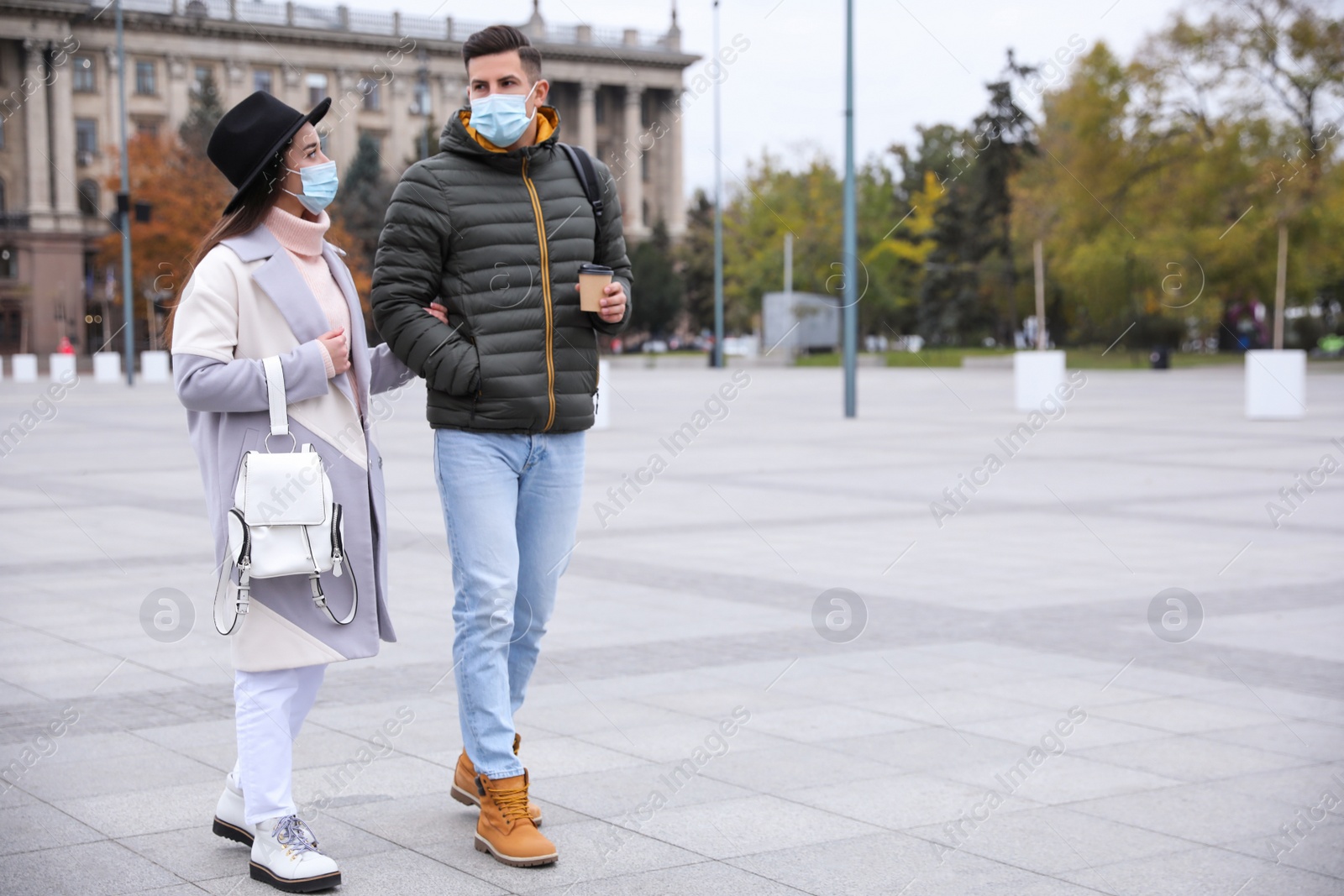 Photo of Couple in medical face masks walking outdoors. Personal protection during COVID-19 pandemic