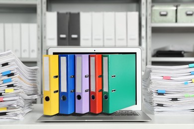 Image of Digital archive. Laptop with folders sticking out of screen in office
