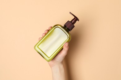 Photo of Woman holding shampoo bottle on beige background, top view