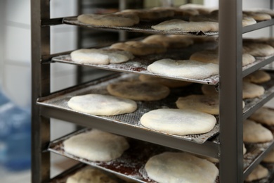 Photo of Rack with unbaked pastries in workshop, closeup