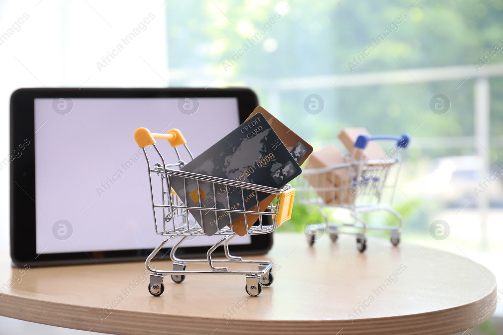 Photo of Internet shopping. Small cart with credit cards near modern tablet on table indoors