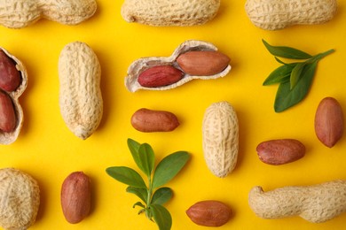 Photo of Fresh peanuts and leaves on yellow table, flat lay