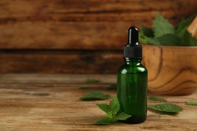 Photo of Glass bottle of nettle oil with dropper and leaves on wooden table. Space for text