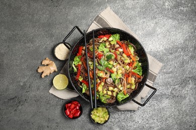 Wok with noodles, mushrooms, vegetables and other products on grey table, flat lay