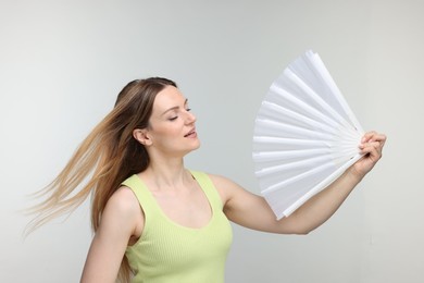 Photo of Beautiful woman waving white hand fan to cool herself on light grey background