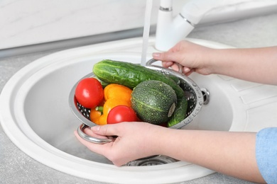 Photo of Woman washing fresh vegetables in colander under water, closeup