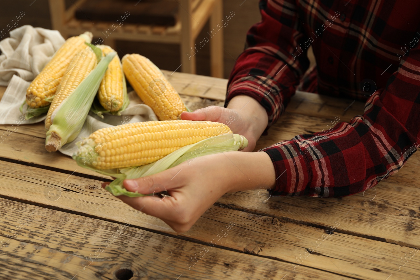 Photo of Woman husking corn cob at wooden table, closeup