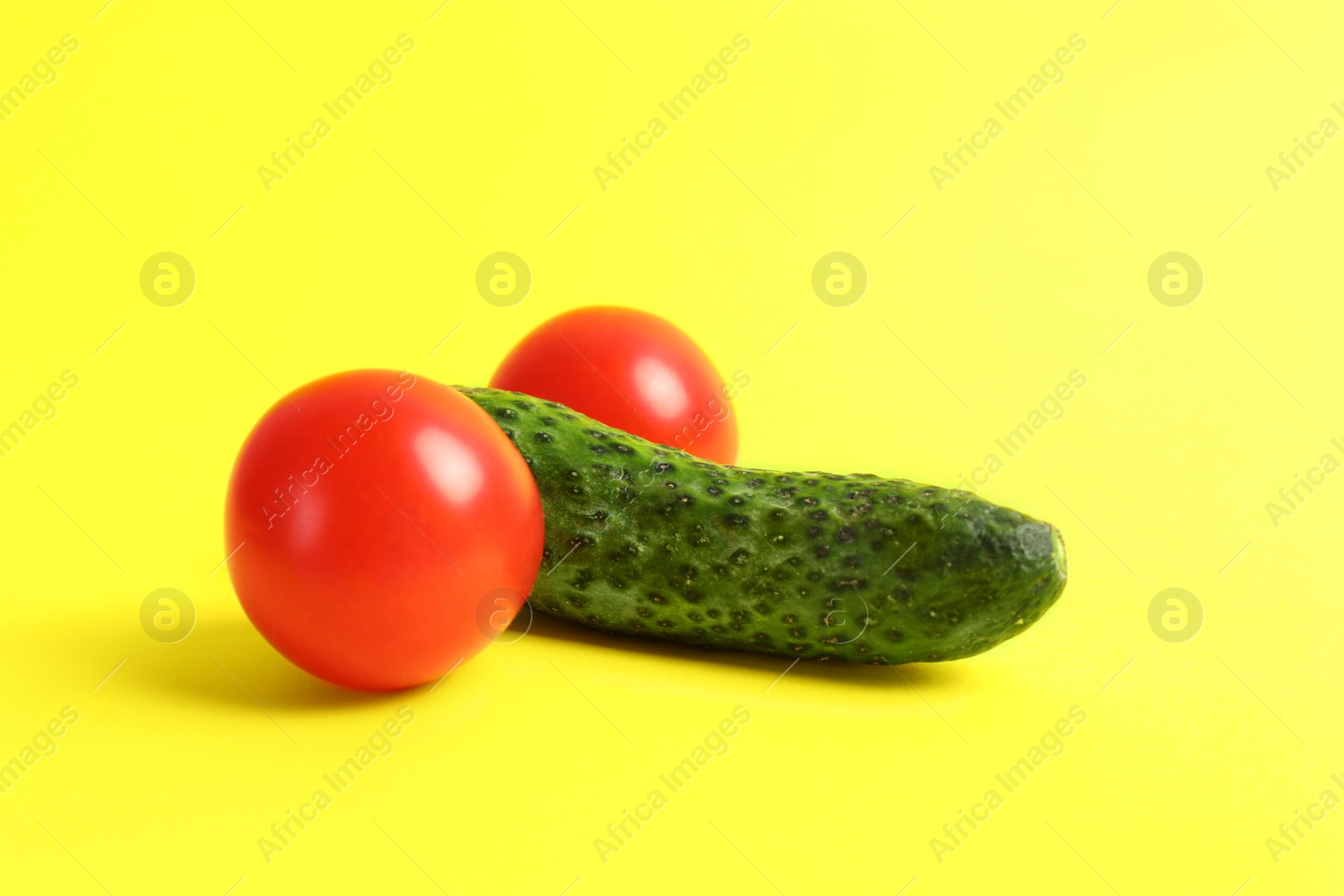 Photo of Cucumber and tomatoes symbolizing male genitals on yellow background. Potency concept
