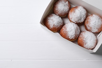 Photo of Delicious sweet buns in box on white wooden table, top view. Space for text