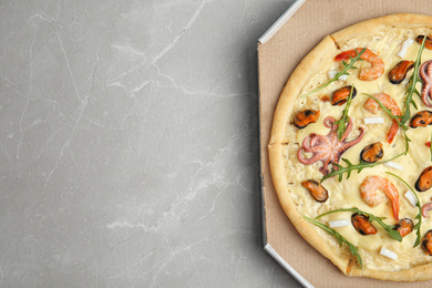 Photo of Delicious seafood pizza  in cardboard box on grey marble table, top view. Space for text