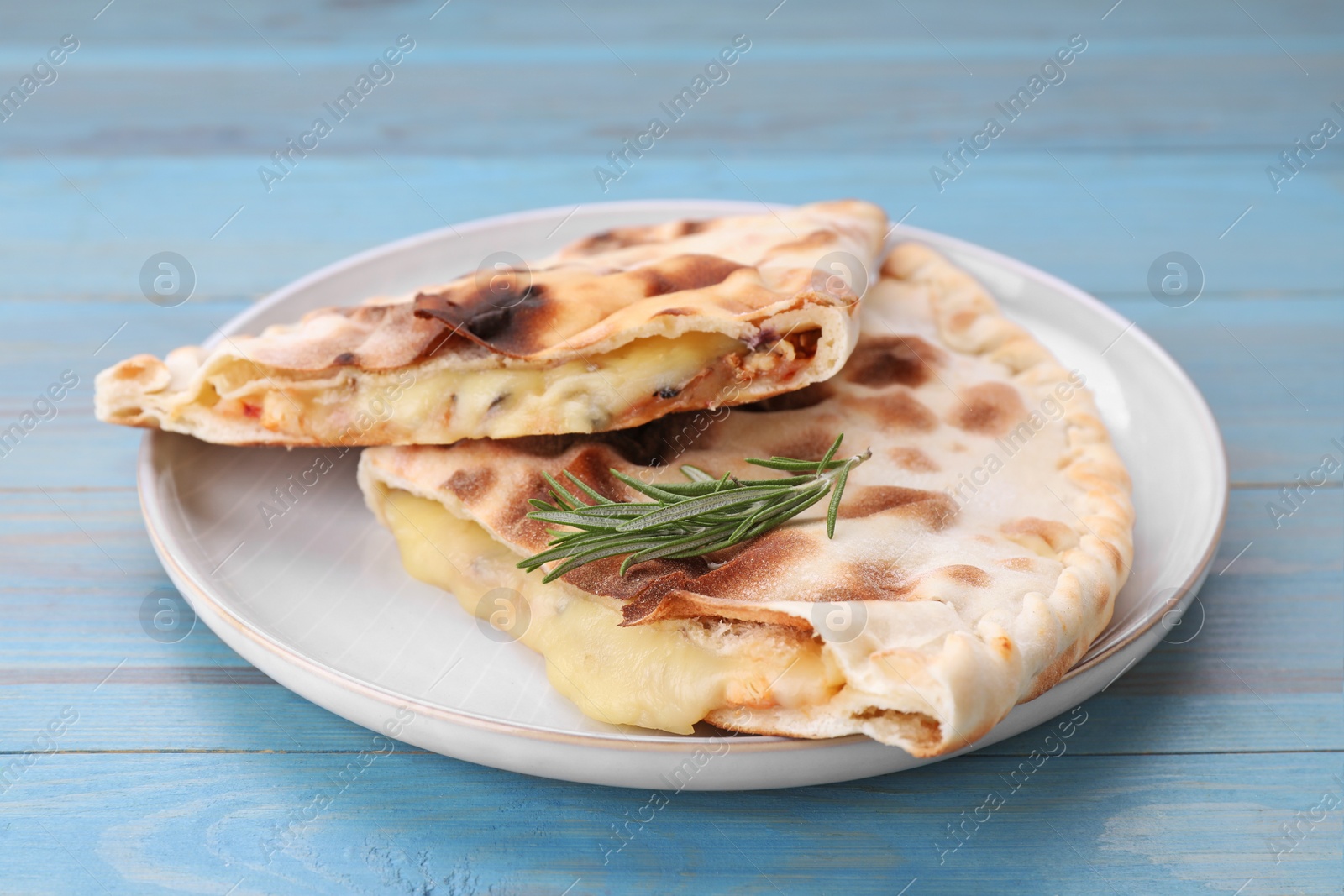 Photo of Tasty pizza calzones with cheese and rosemary on light blue wooden table, closeup