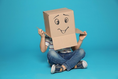 Photo of Cute little child wearing cardboard box with smiling face on color background