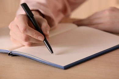 Photo of Woman writing in notebook at wooden table, closeup