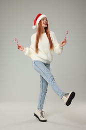Photo of Young woman in Santa hat with candy canes on light grey background. Christmas celebration