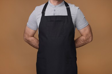 Photo of Man wearing kitchen apron on brown background, closeup. Mockup for design