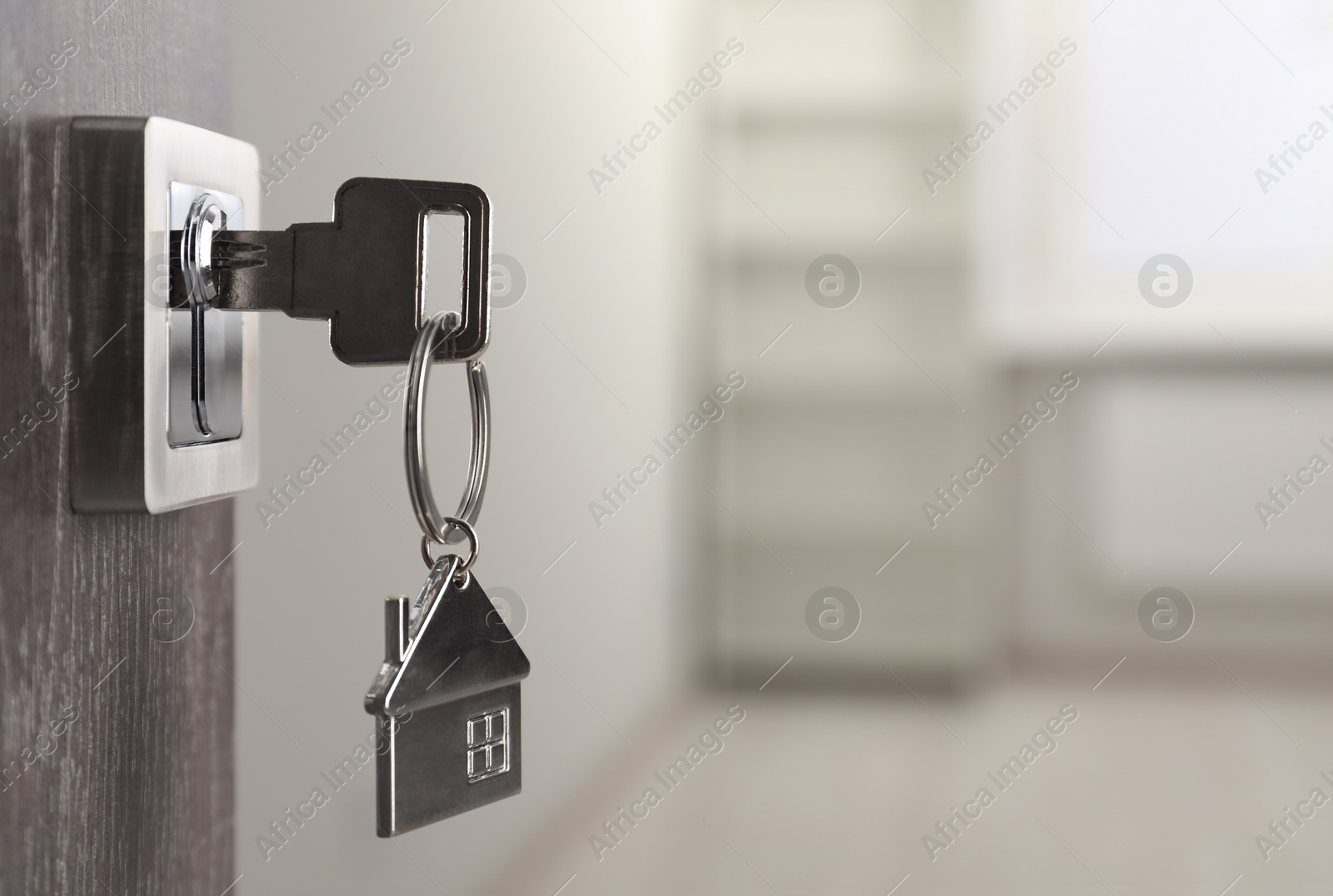 Photo of Mortgage and real estate. Open door with key and house shaped keychain against blurred background, space for text