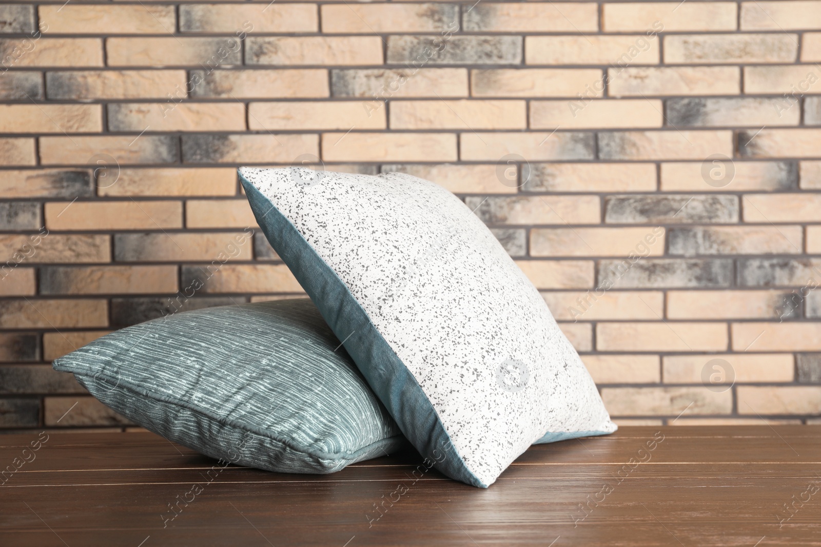 Photo of Soft decorative pillows on table against brick wall background