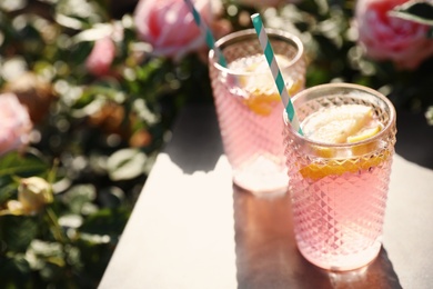 Photo of Glasses of pink rose lemonade on  table in blooming garden. Space for text