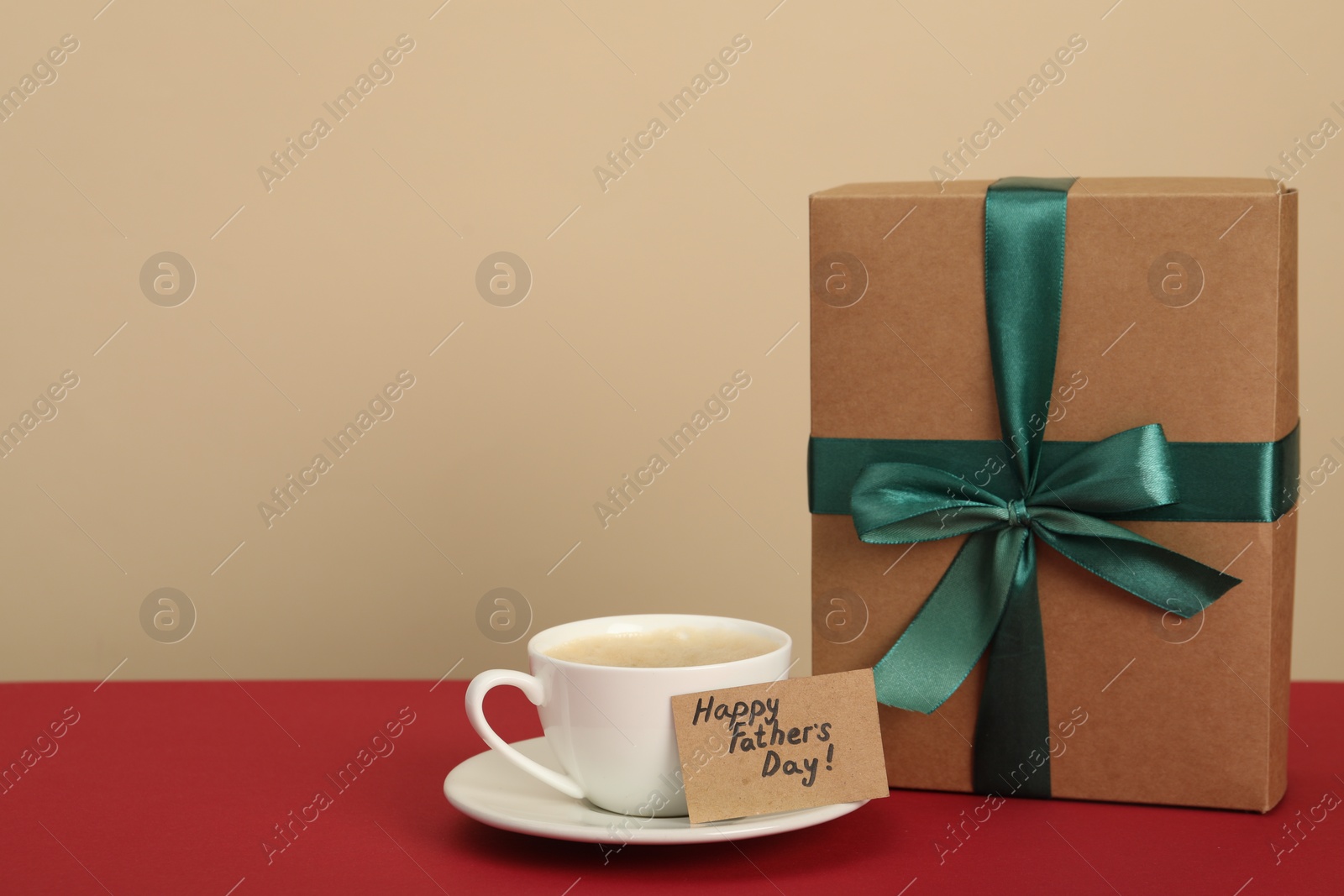 Photo of Happy Father's Day. Coffee cup, card with greetings and gift box on red table. Space for text