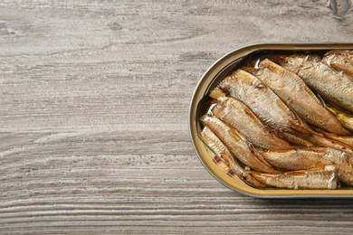 Photo of Open tin can of sprats on wooden background, top view. Space for text
