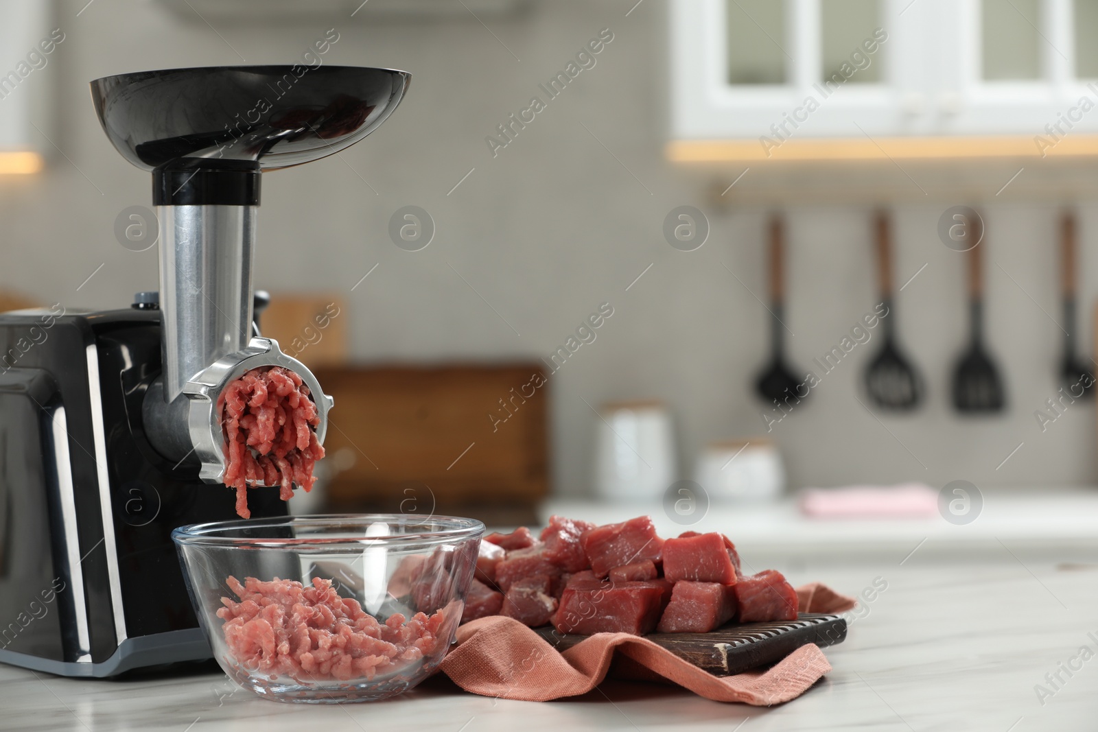 Photo of Electric meat grinder with beef mince on white table in kitchen, space for text